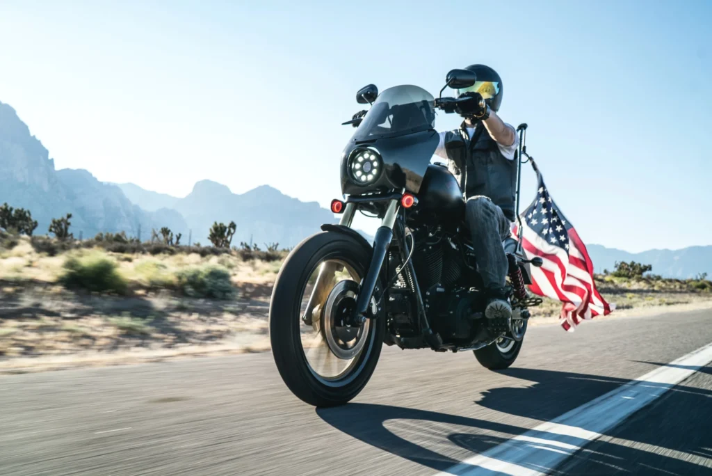 A motorcyclist riding on a desert highway with an American Flag Can You Bring a Motorcycle Accident Injury Claim in Georgia If You Were Not Wearing a Helmet?